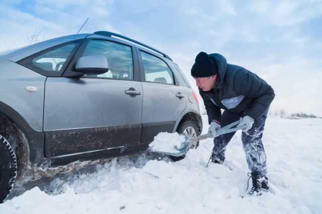 Man shoveling snow to free his stuck car